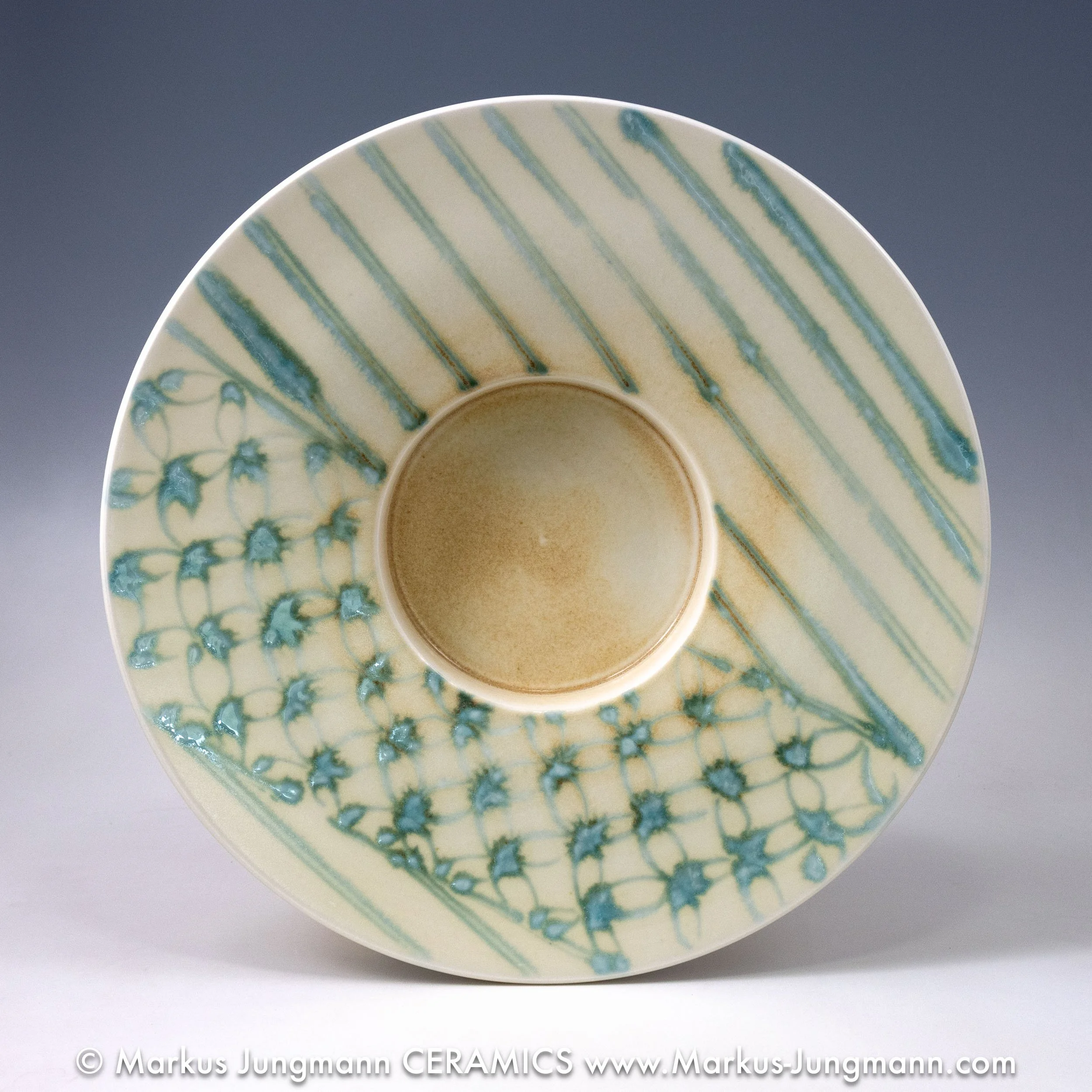 Wide-rimmed porcelain bowl with diagonal teal stripes and an inset net pattern on a cream ground, by Markus Jungmann. top view.
