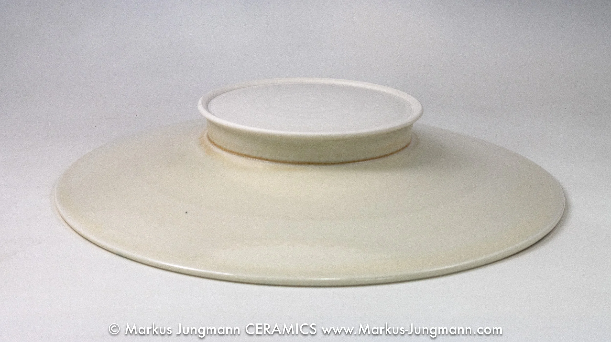 Wide-rimmed porcelain bowl with diagonal teal stripes and an inset net pattern on a cream ground, by Markus Jungmann. bottom view.