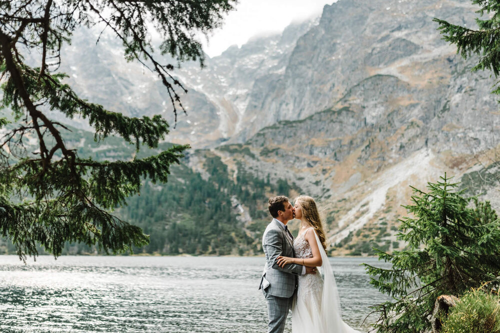 https://images.squarespace-cdn.com/content/v1/597282dd6b8f5bd129c3ae8c/1592317608070-2DSL32XRPN004DE1LHDS/bride+and+groom+kissing+at+beautiful+outdoor+wedding+venues+with+lake+and+mountains.jpg?format=1000w