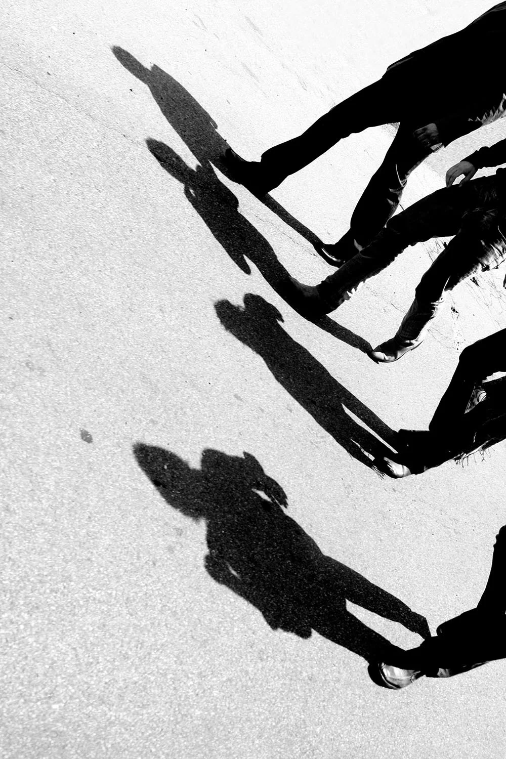 Black and white photograph of four men casting shadows on the street while walking.