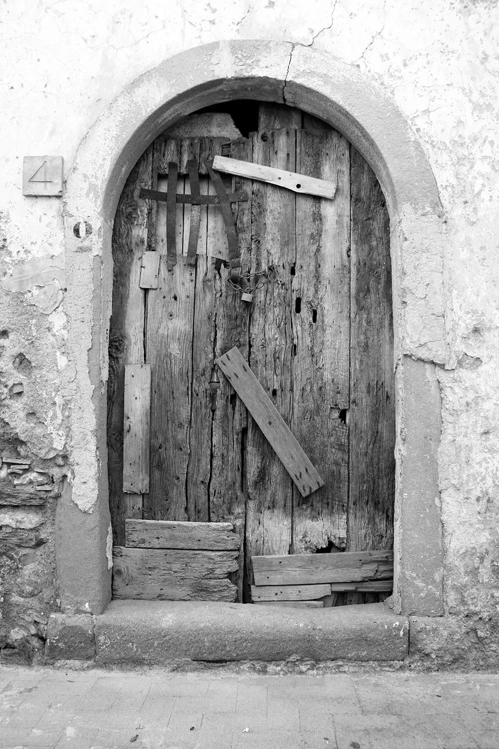 Black and white photo of an old wooden door nailed shut with plywood.