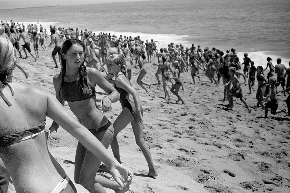 Black and white photo of a beach covered in running, screaming children.