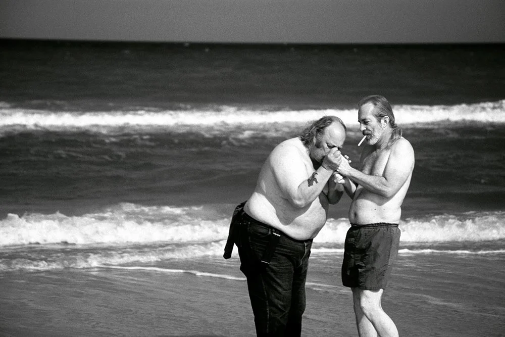 Black and white photograph of two old men smoking cigarettes at the beach.