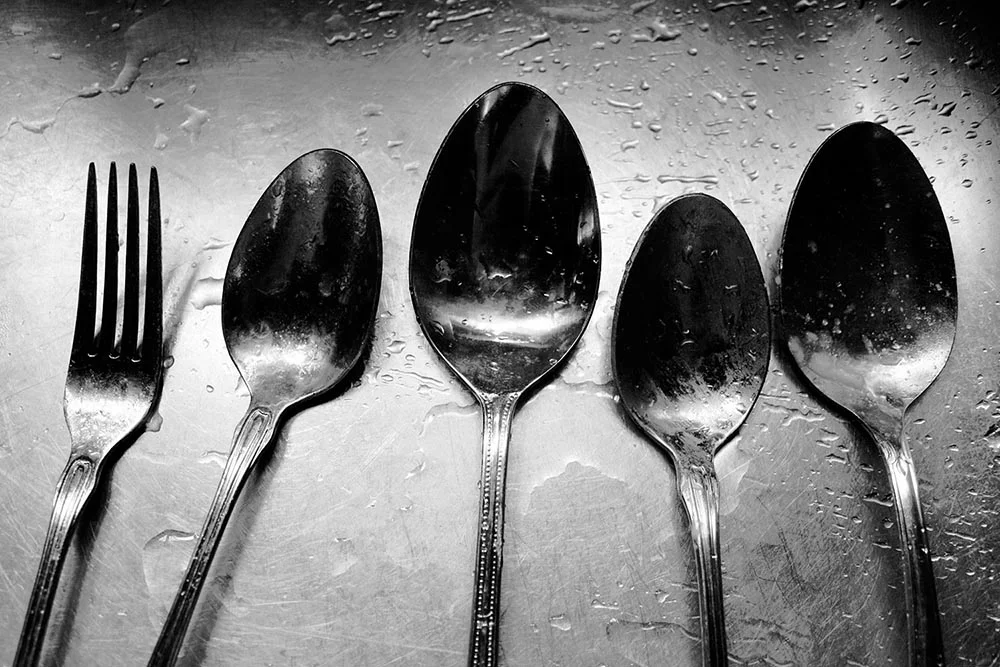 Black and white photograph of four mismatched spoons and a solitary fork.