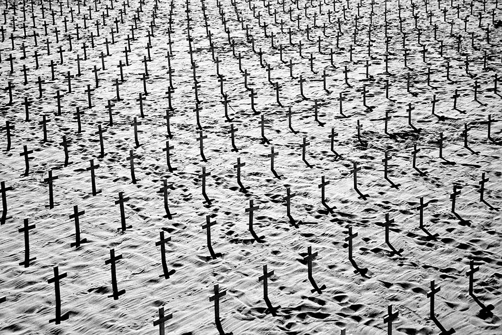 Black and white photograph of silhouetted wooden crosses on a beach.