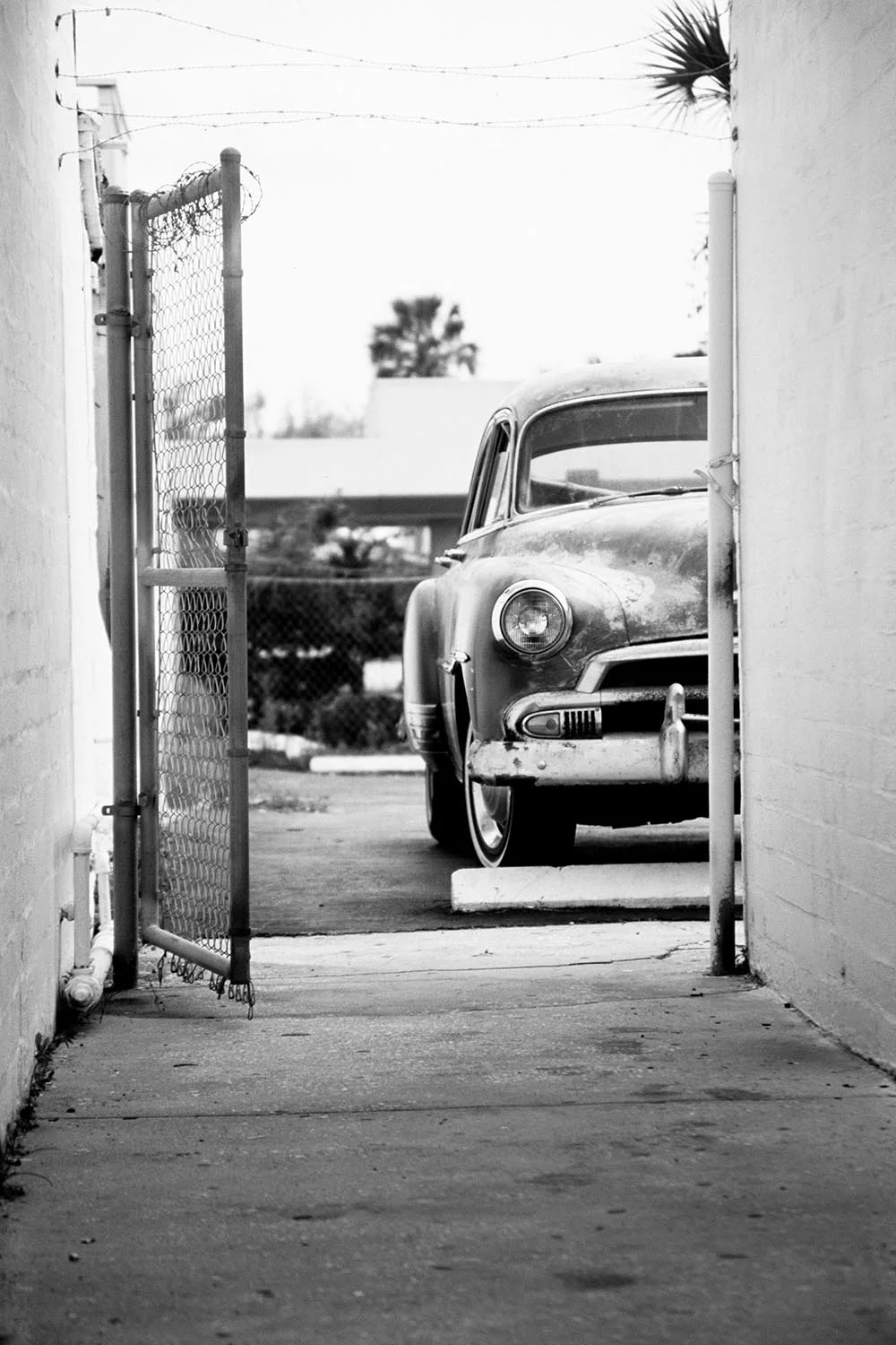 Black and white photograph of an antique car half-seen down an alley way.