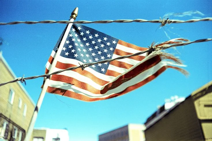 An American flag caught on barbed wire, photographed on Fuji Provia 100F and cross-processed.