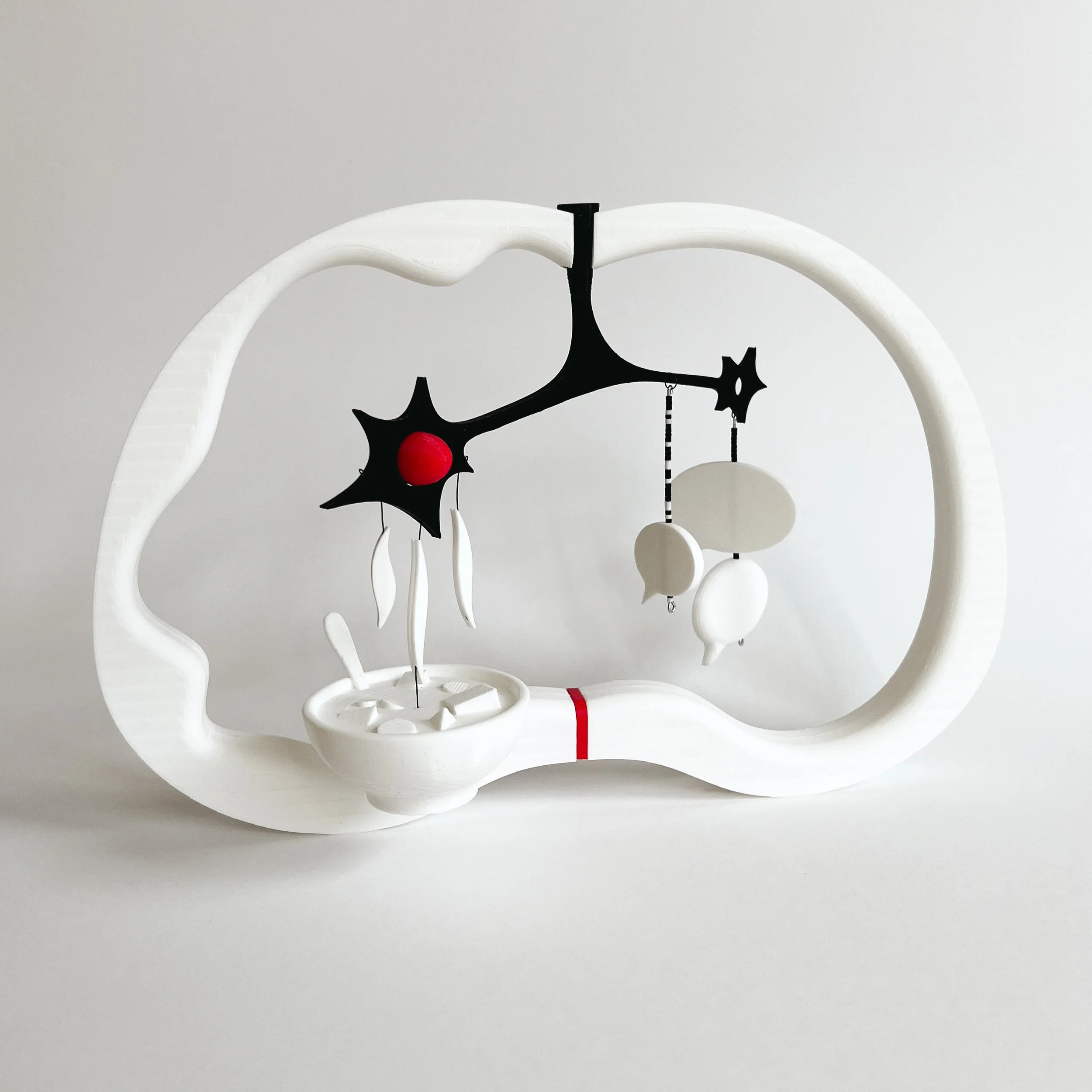 A modern, abstract mobile sculpture with a white, irregularly shaped frame, black and white hanging elements, and a red sphere, resembling a brain with cellular structures.