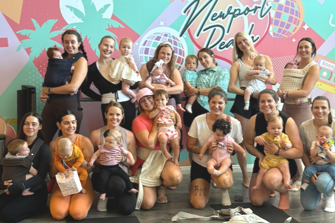 Group of women holding babies at Newport Baby event with colorful tropical-themed backdrop.
