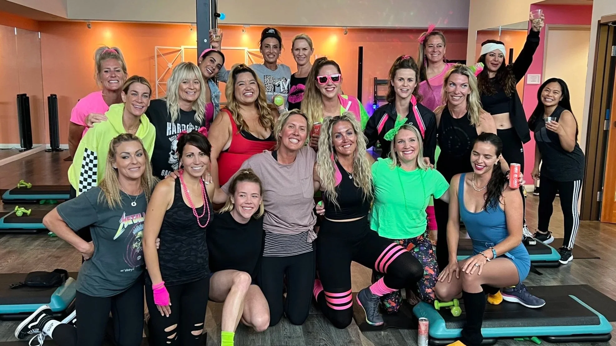 Group of women in bright, colorful workout clothing celebrating after a fitness class in a gym studio.