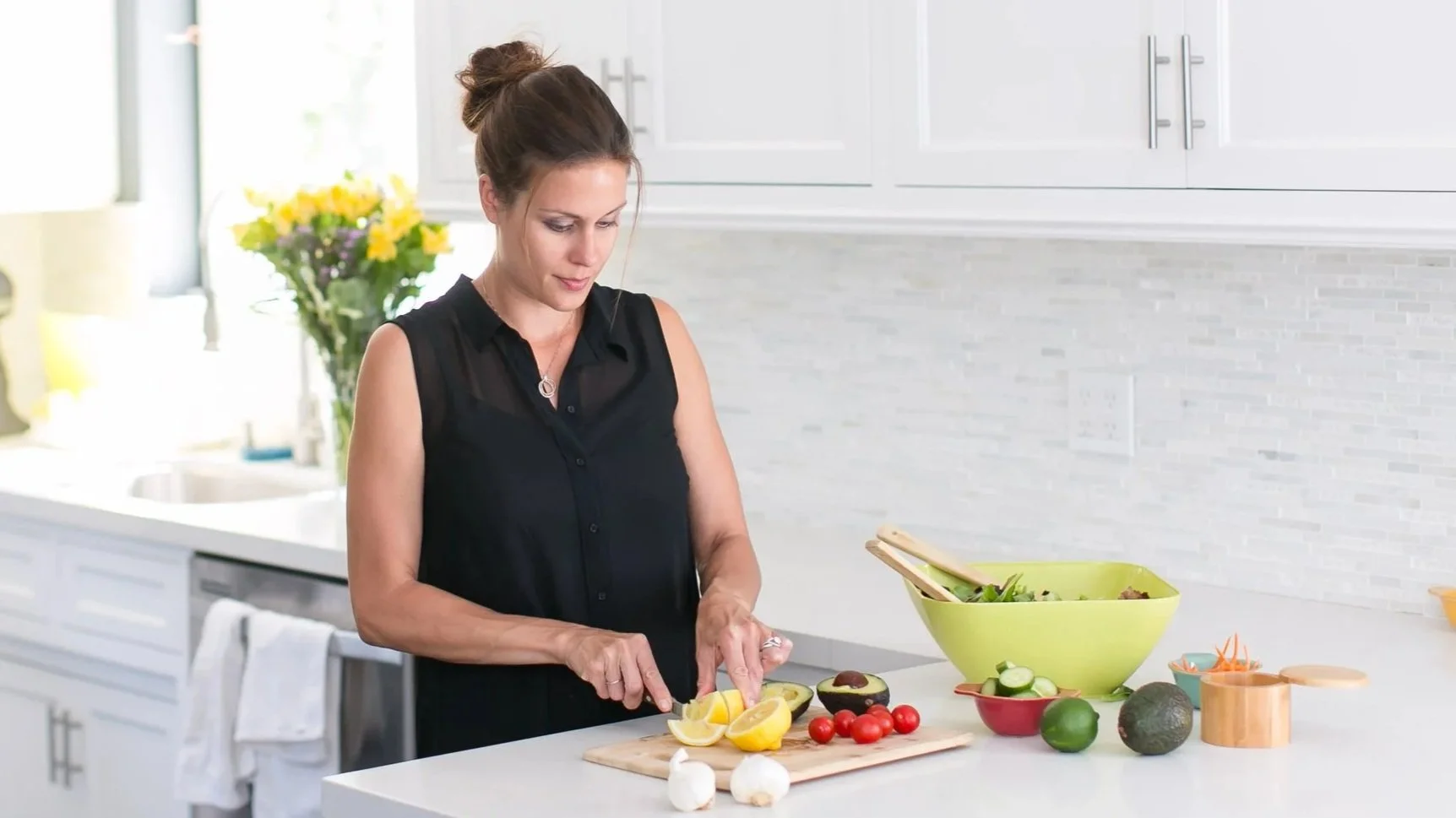 Woman chopping lemons in a modern kitchen with fresh vegetables and fruits on the counter
