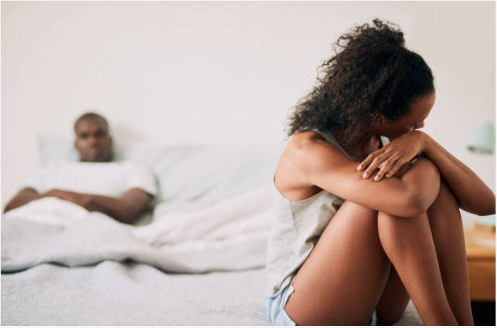 african american couple sitting on opposite sides of the bed. Male partner upset and female partner upset with back tu