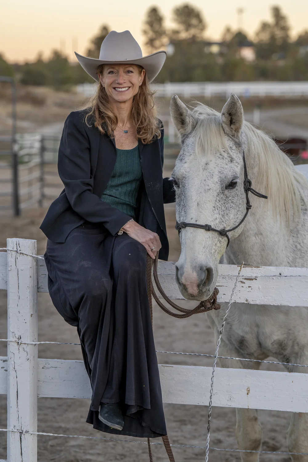 Michelle Kaye seated on a fence beside a white horse