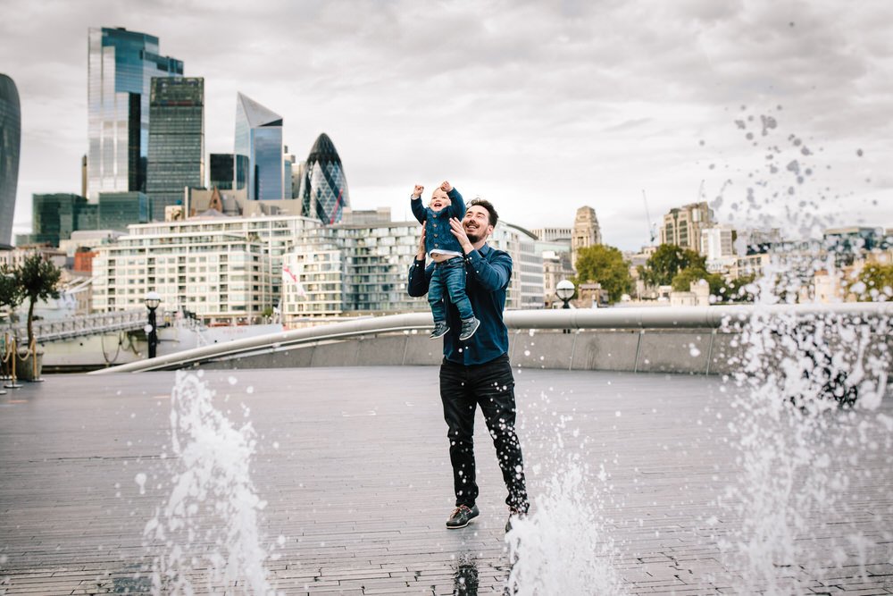 Father and son play in the fountains by Tower Bridge with views of the city of London