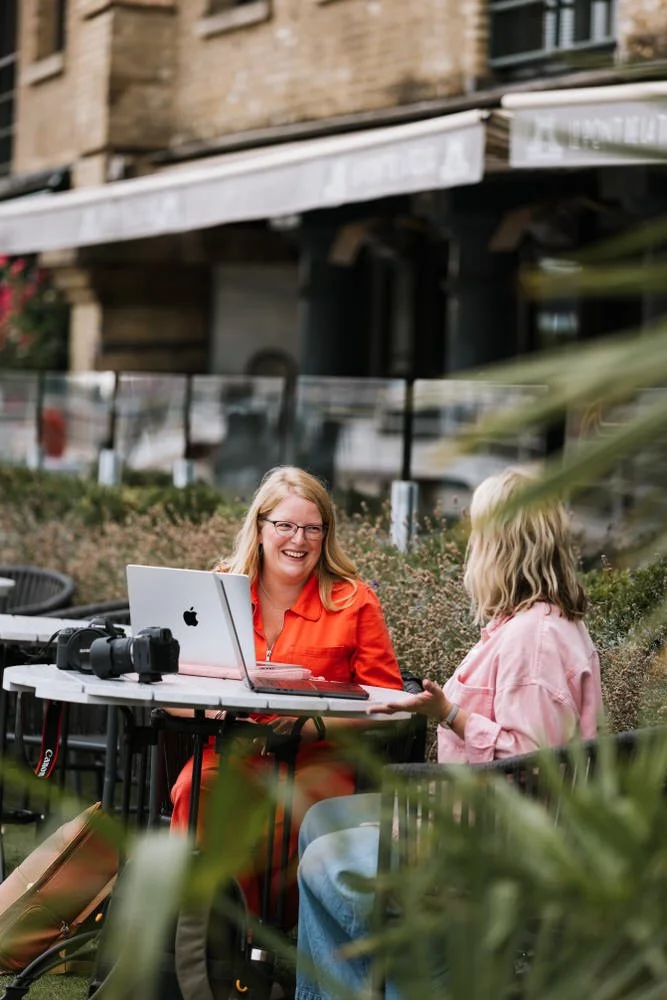 Kirsty Hamilton Photography Business Mentor smiles across her open laptop as she teaches a photographer