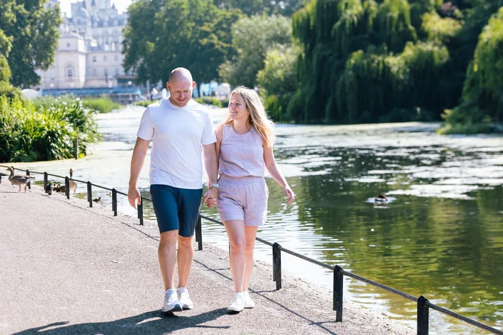 Couple stroll next to pond after romantic proposal in St James Park
