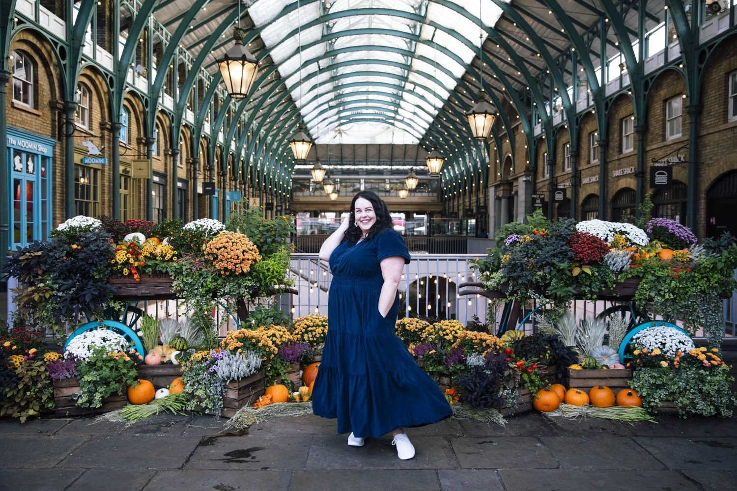 Woman in blue dress spins infront of seasonal floral display in Covent Garden