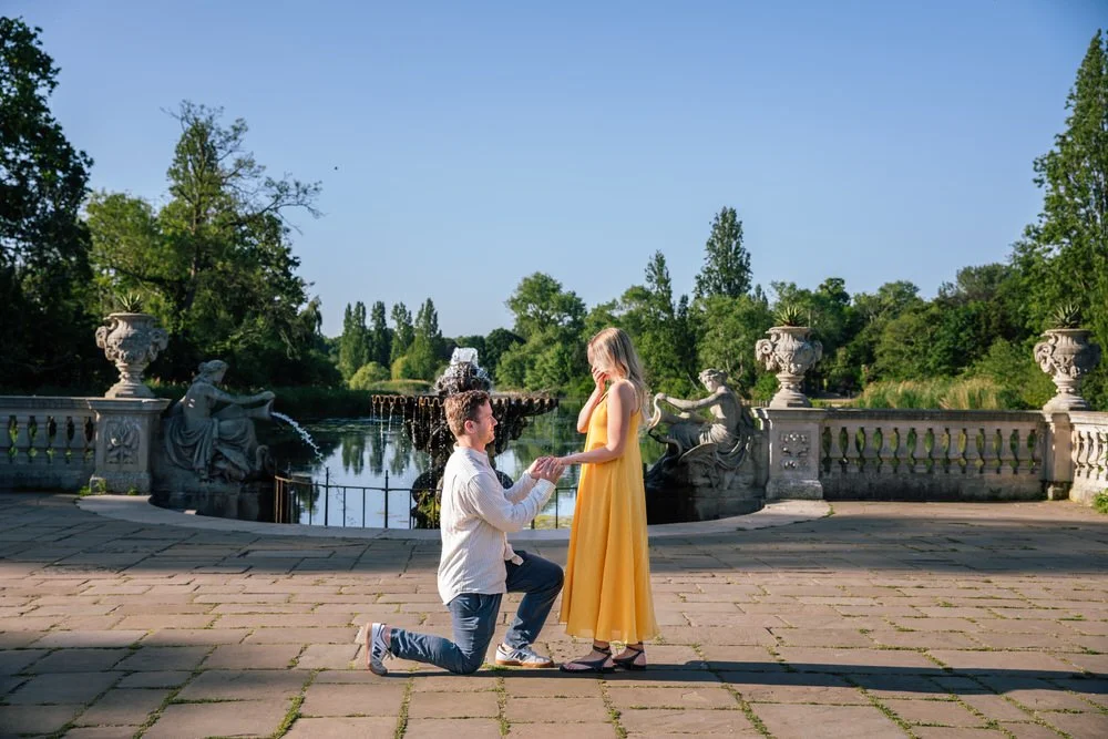 Woman in yellow sun dress in shock after her boyfriend proposes in the Italian Water Gardens in Hyde Park