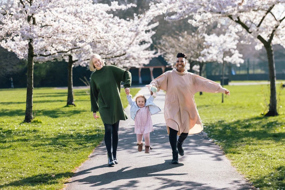 Two mums swing their toddler down the avenue of cherry blossom trees in Battersea Park