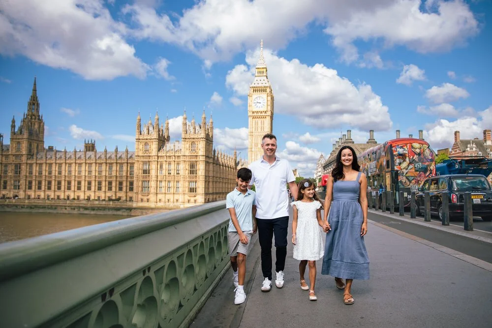 A family of four walking along Westminster Bridge with Big Ben and the Houses of Parliament in the background in London, England. Captured by a London Family photographer