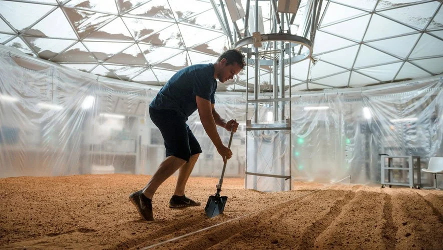 Here Mark Watney wearing shorts — who oddly moves as if he still weighs what he did on Earth — is using a shovel to kick up toxic perchlorate-ridden micro-dust in order to study the effects such indoor farm work has on his lungs. Though he may be suffering from radiation-induced dementia and has no idea what he's doing, or perhaps is a little light-headed from the bits of hydrazine that may have failed to catalyze into hydrogen and nitrogen from his water-vapor device. Of course, he might asphyxiate as the flame burns up his oxygen supply... or starves as the potato plants die from the heat generated out of the chemical reaction of his hydrazine-to-water device... but what do I know?