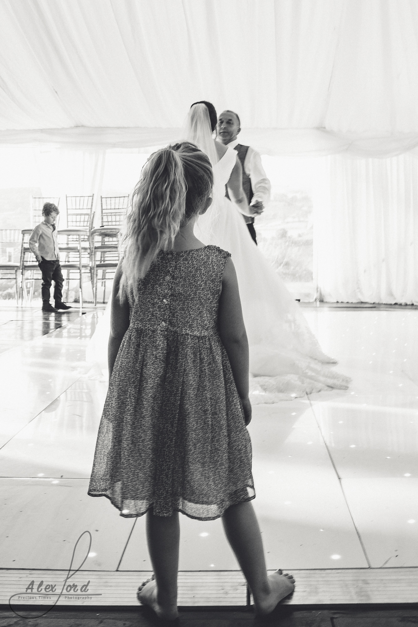 A young girl wedding guest stands at the edge of the dance floor watching the bride and groom take their first dance. 
