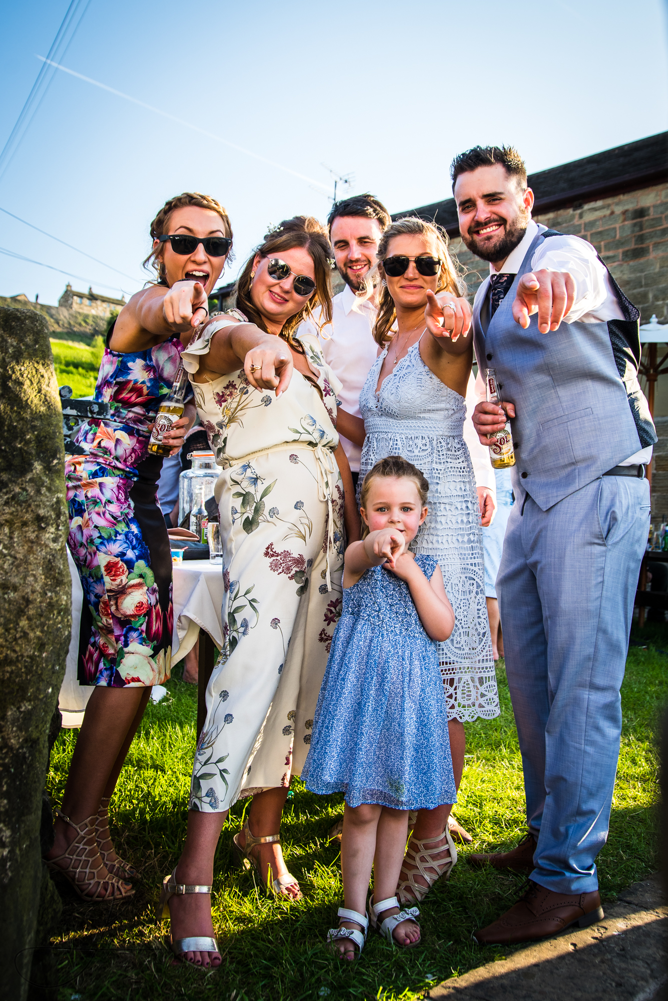 Six wedding guests pose together for a funny photo together, they are dressed in really bright summer wedding clothes