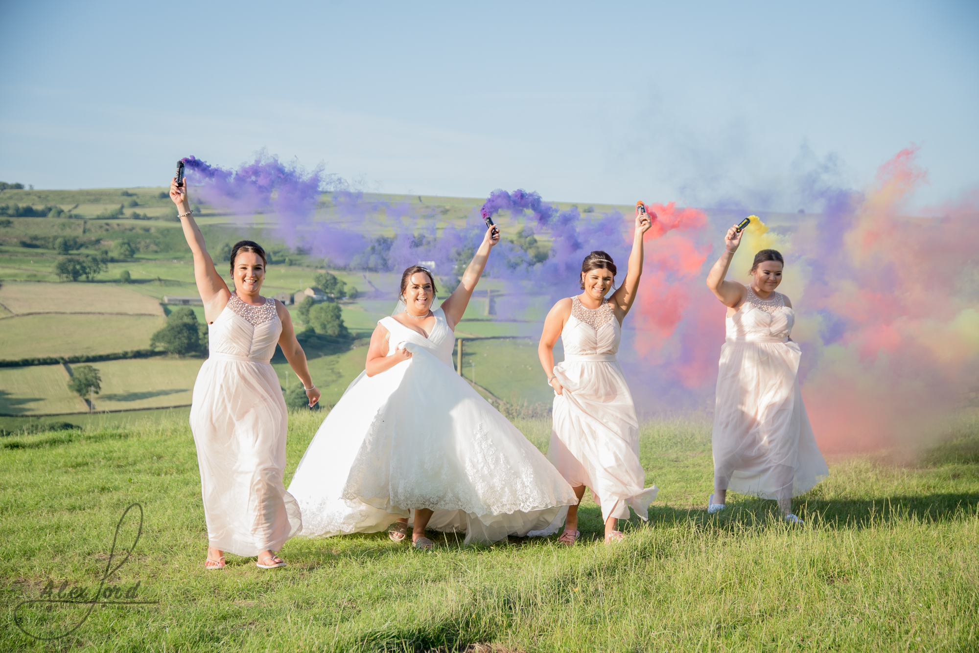 Bride and bridesmaids run wit smoke bombs in a field with the Yorkshire countryside in the background