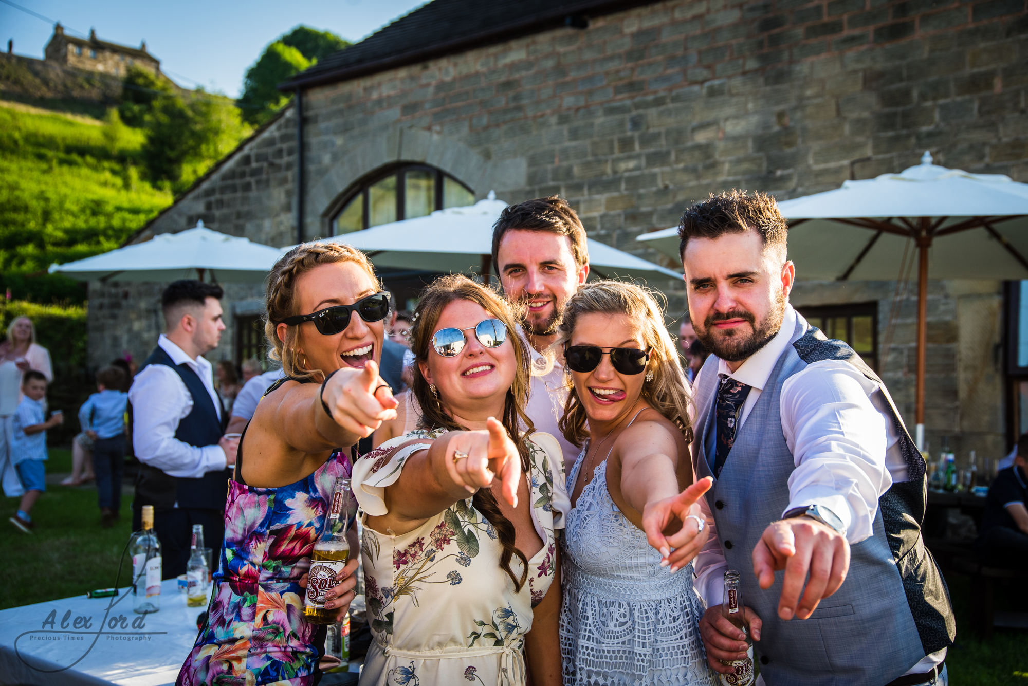 Five wedding guests point towards the camera with really big smiles on their faces