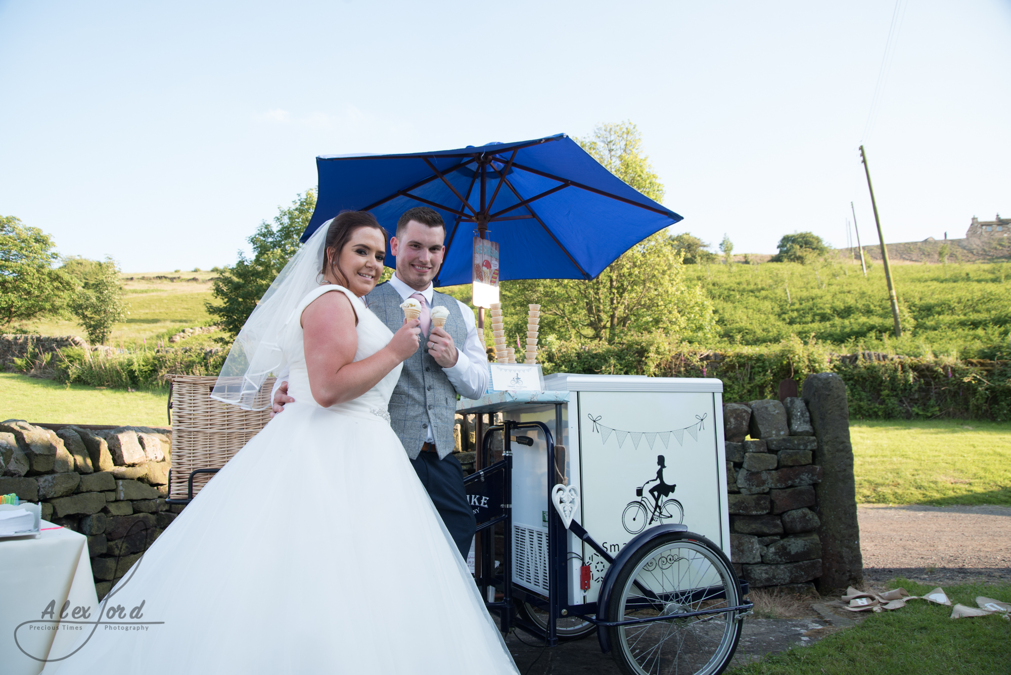 The bride and groom pose with an ice cream in front of their ice cream cart