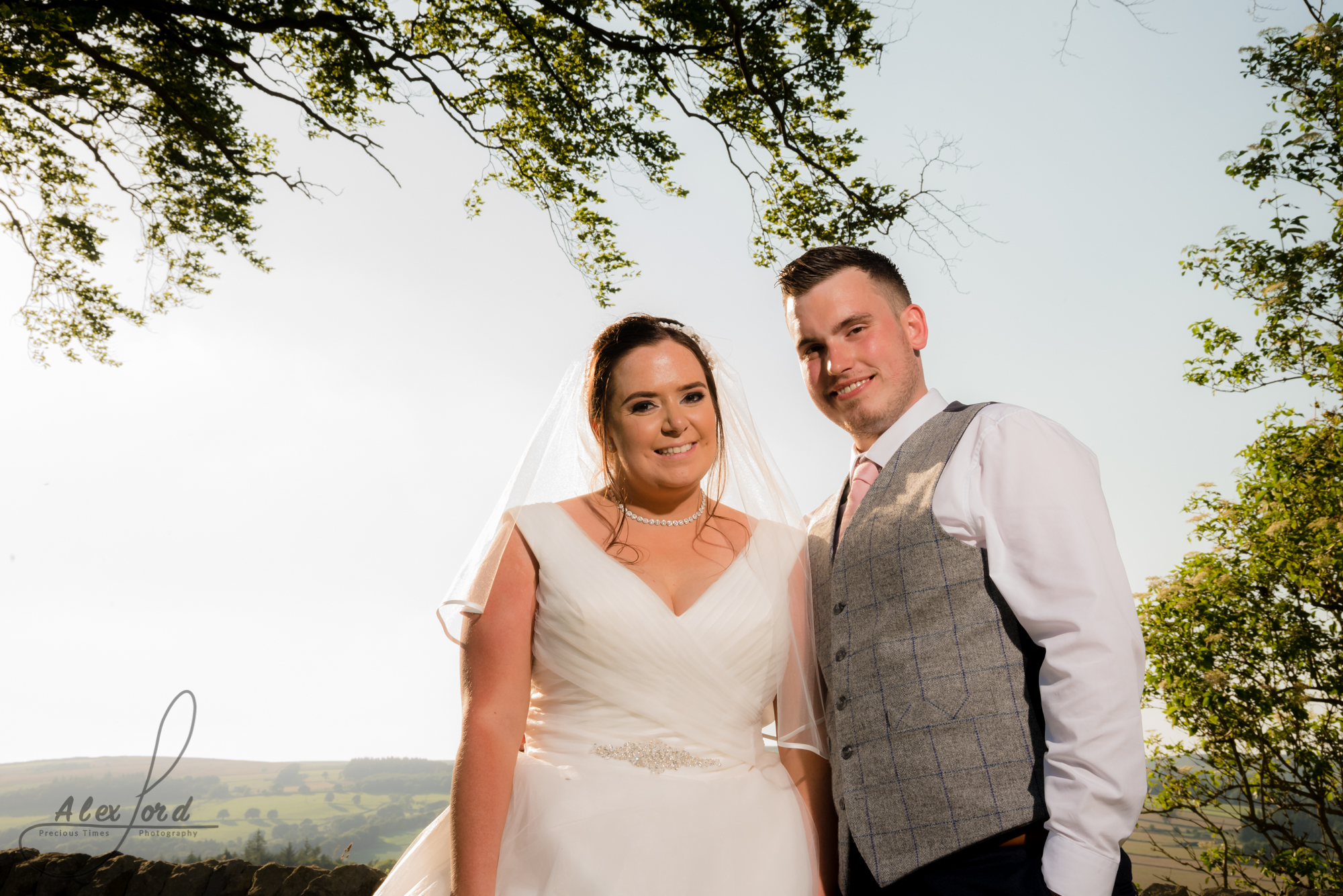 The smiling bride and groom stand in front of a large open sky and the Yorkshire countryside