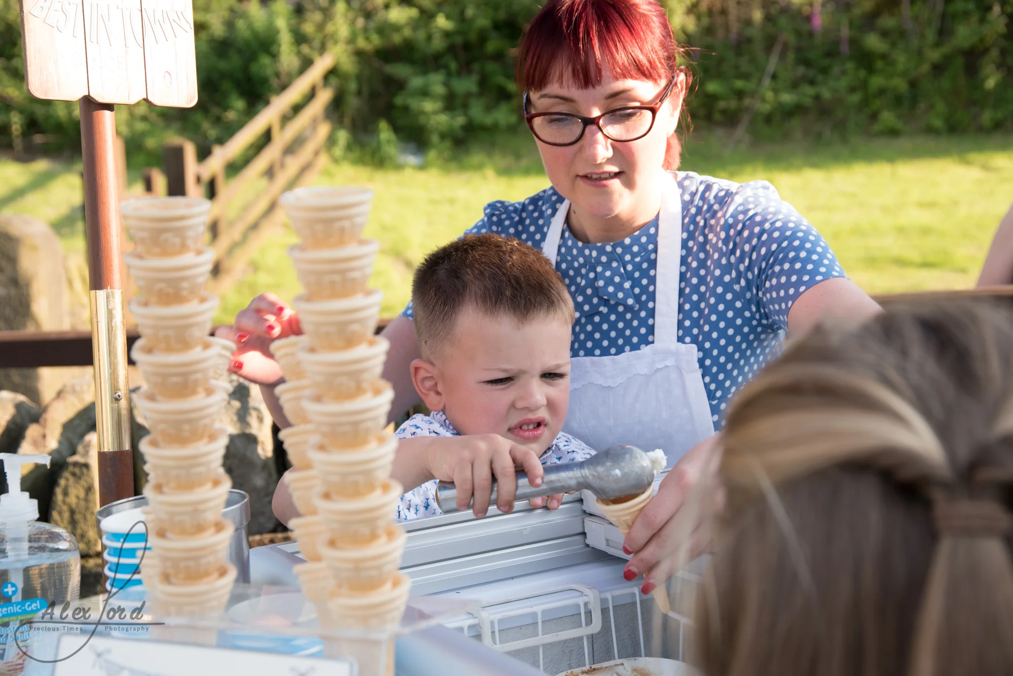A young boy wedding guest puts toppings on their ice cream