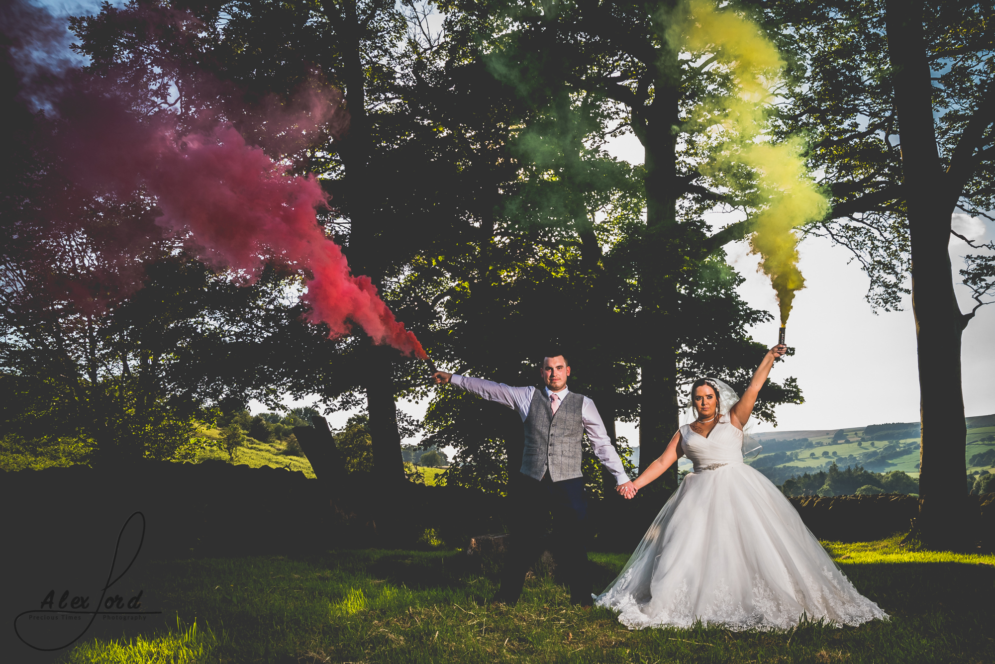 The bride and groom hold coloured smoke bombs while they pose for their wedding photo 