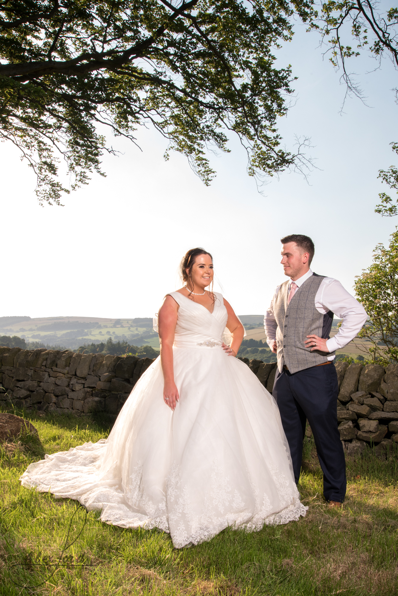 The bride and groom stand in the summer sunlight