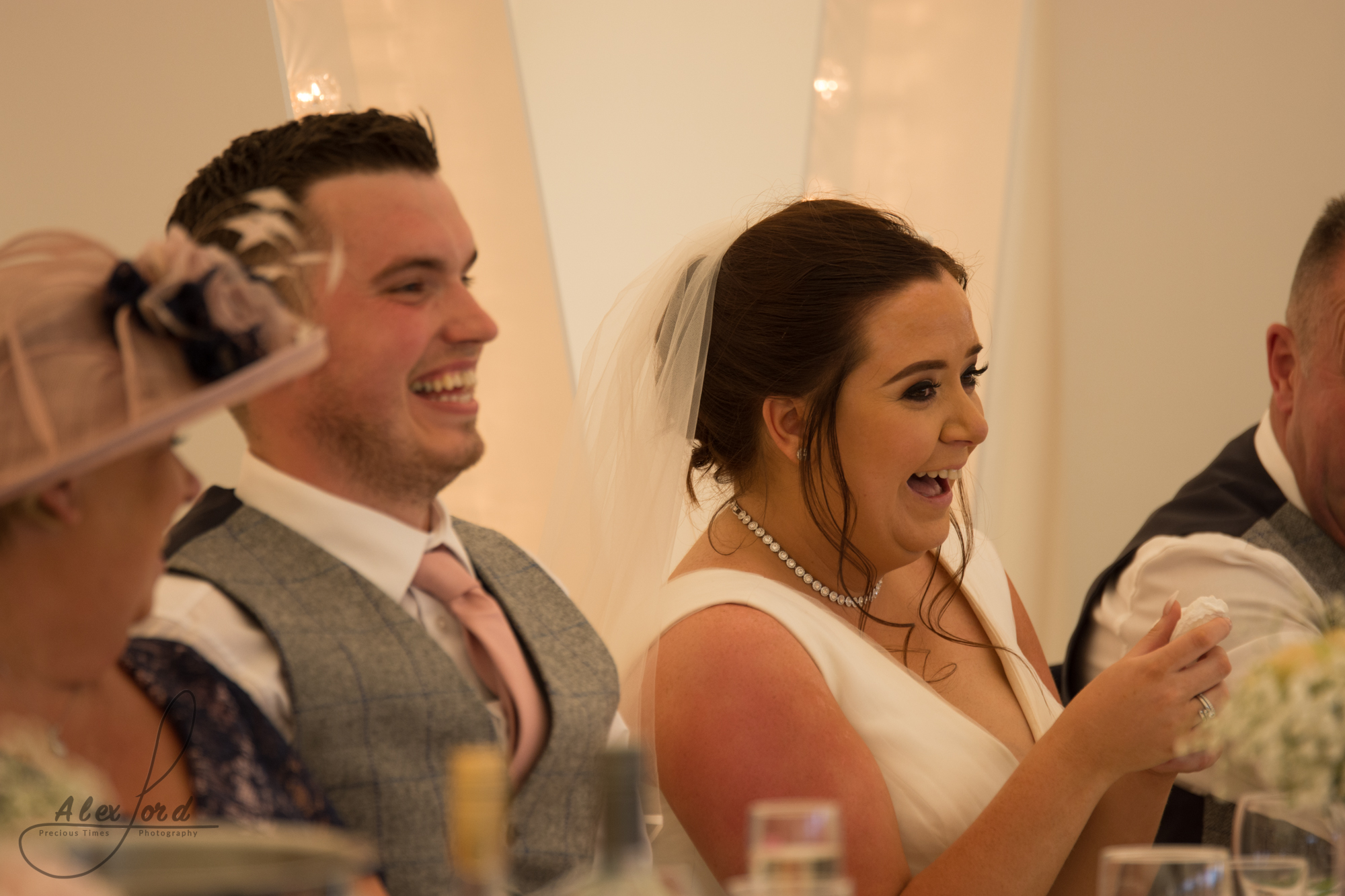 Bride and groom laugh out loud at a joke during the wedding speeches