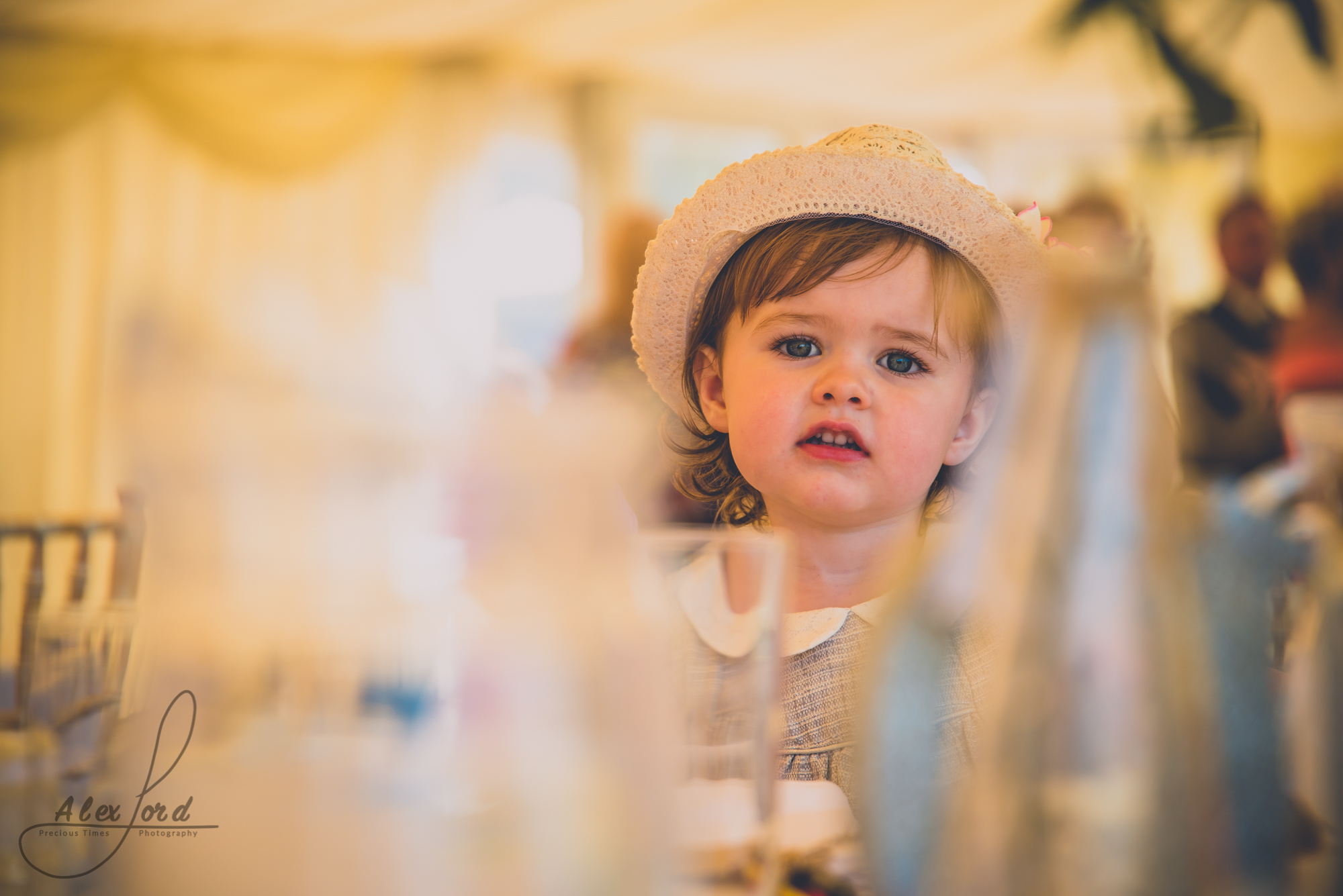 A young girl wedding guest sits at a table at ding breakfast, partly hidden by the glasses on the table