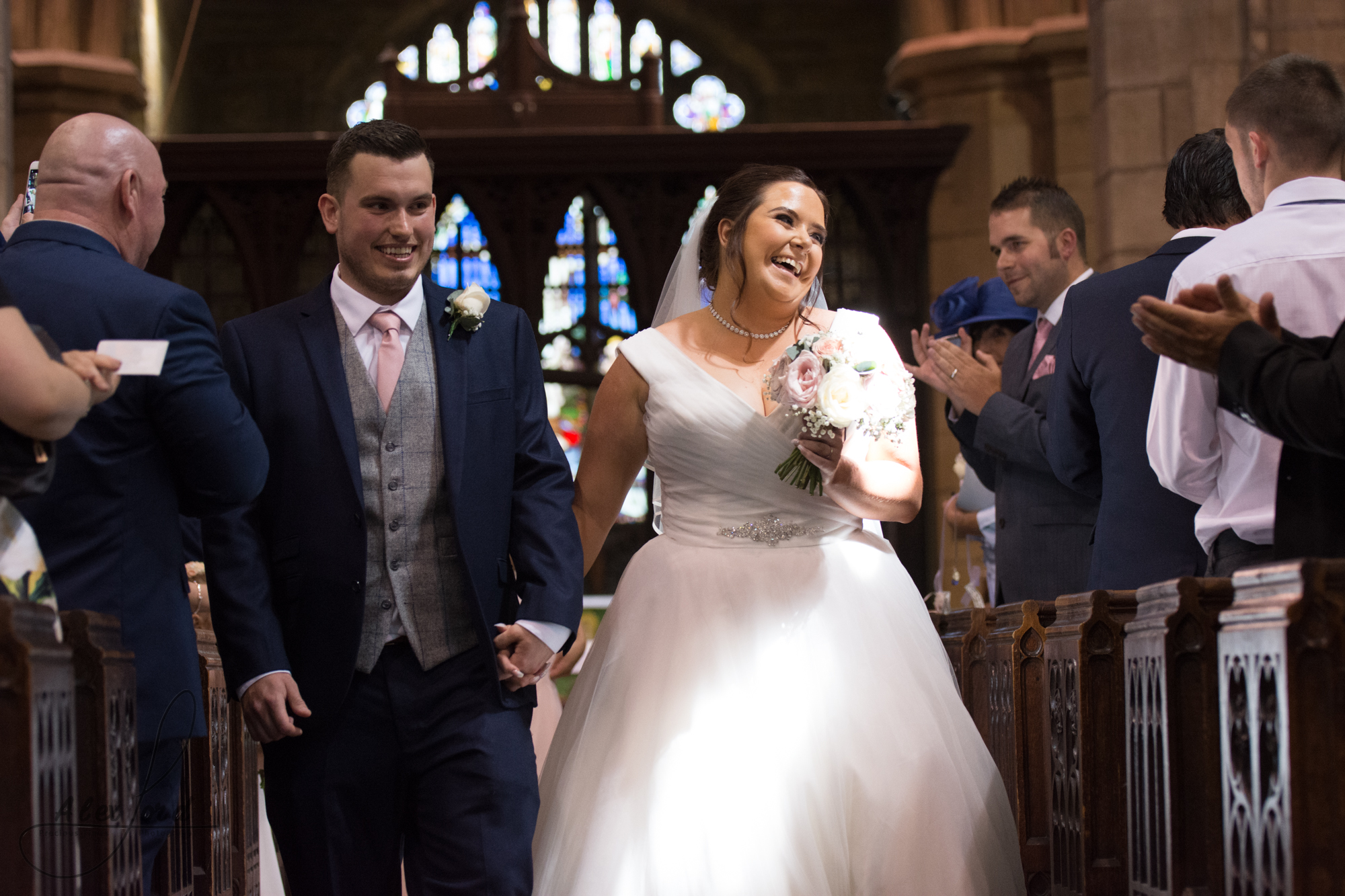 The bride and groom exit the church together with big smiles on their faces, straight after their wedding service