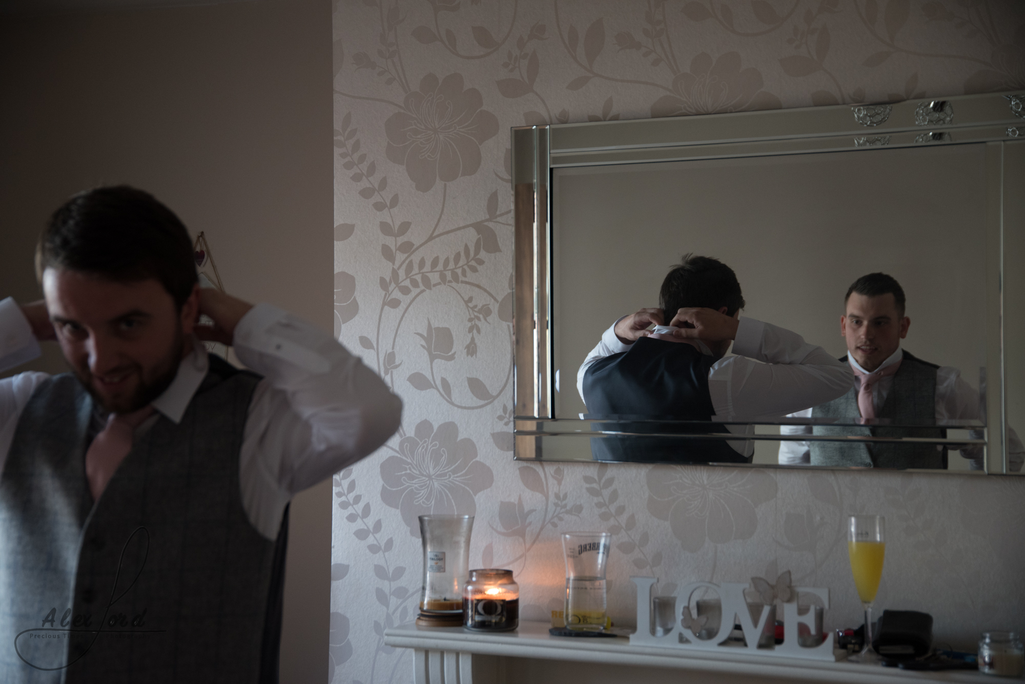 The groom and the best man dressed in blue suits finish tying their ties before leaving for the wedding ceremony