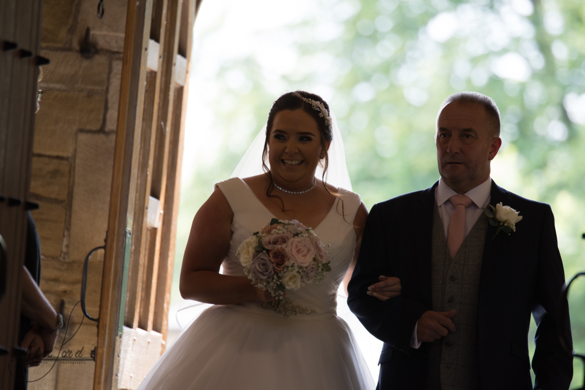 The bride dressed in a stunning princess dress with a big smile on her face walks into the church with her father on her arm