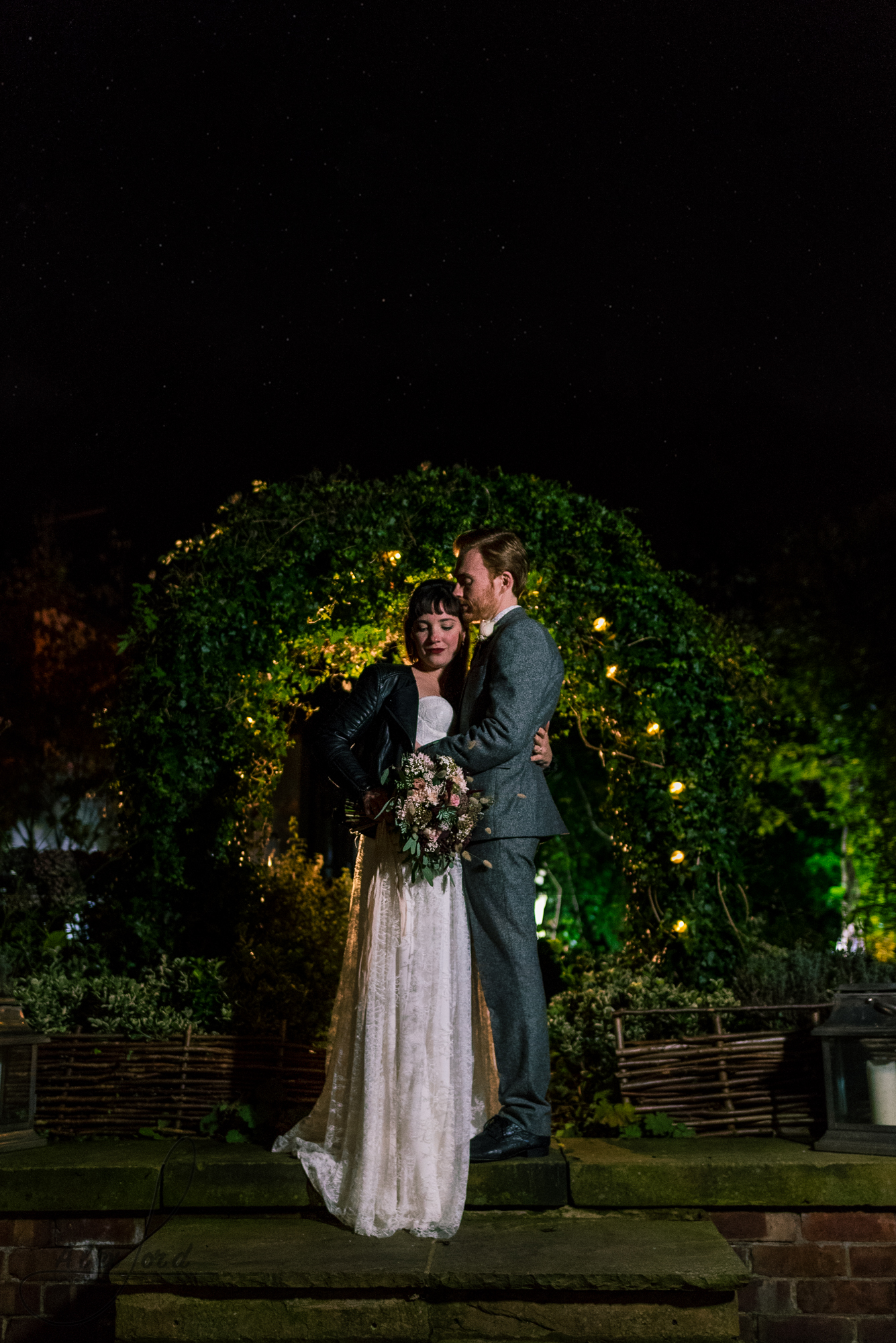 bride and groom stand under a bushy archway for some nighttime photography with the flash