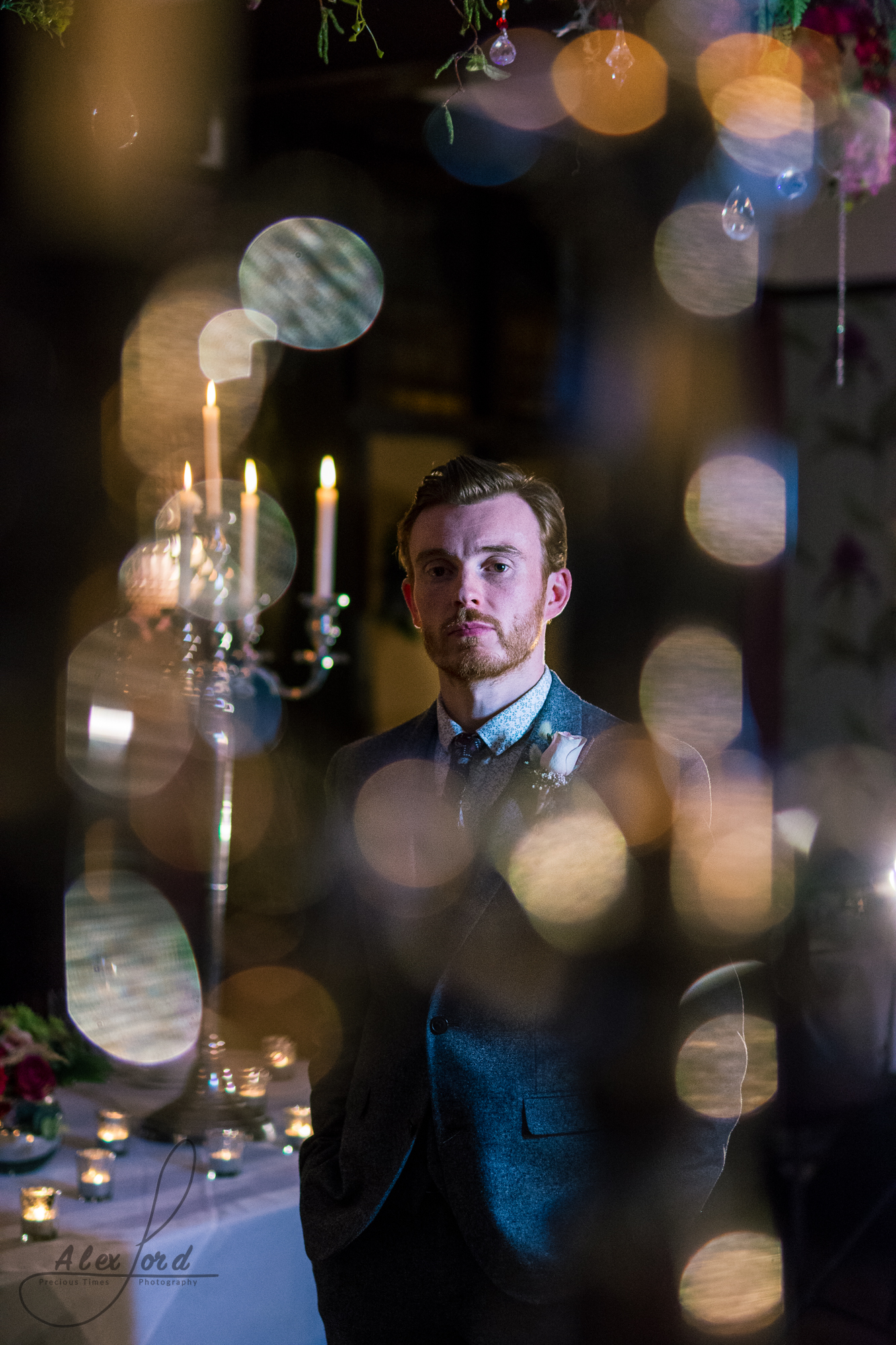 inside the wedding venue the groom stand on his own surrounded by candles in dim light