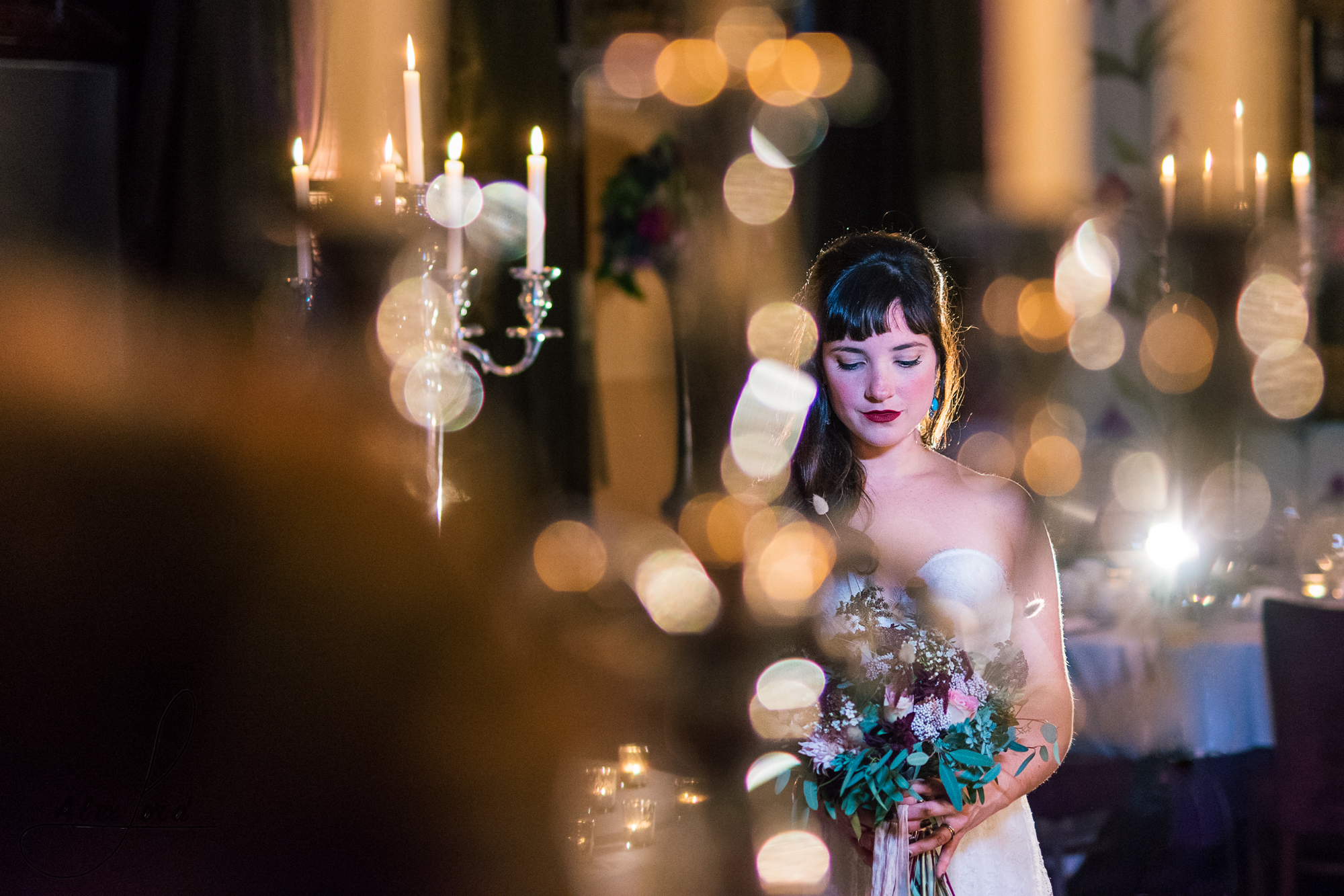 the bride is standing on her own surrounded by candles in her wedding venue in cheshire, lit only with a single light