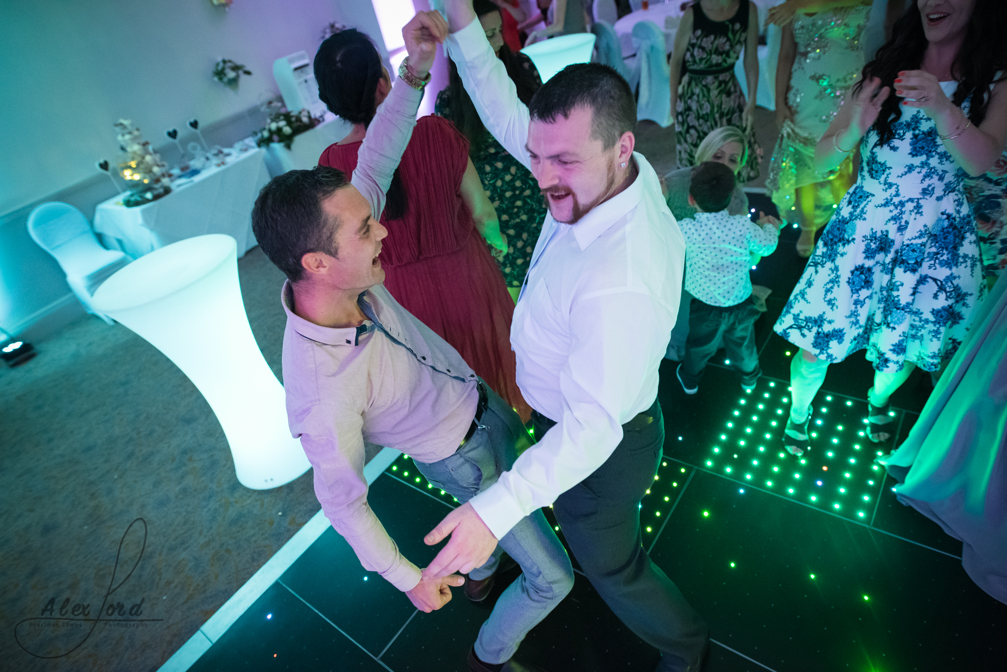 two male wedding guests on the dance floor with their arms up in the air