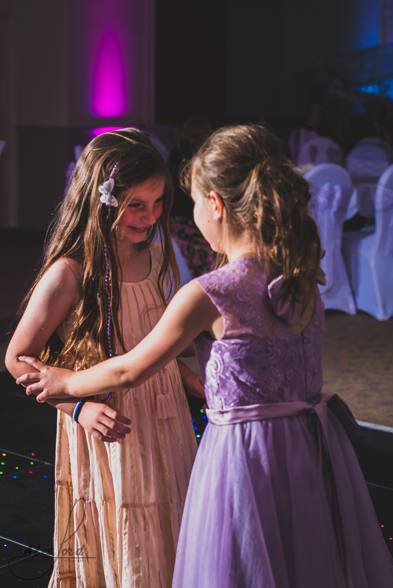 two young girl wedding guests hold hands and dance on the dance floor