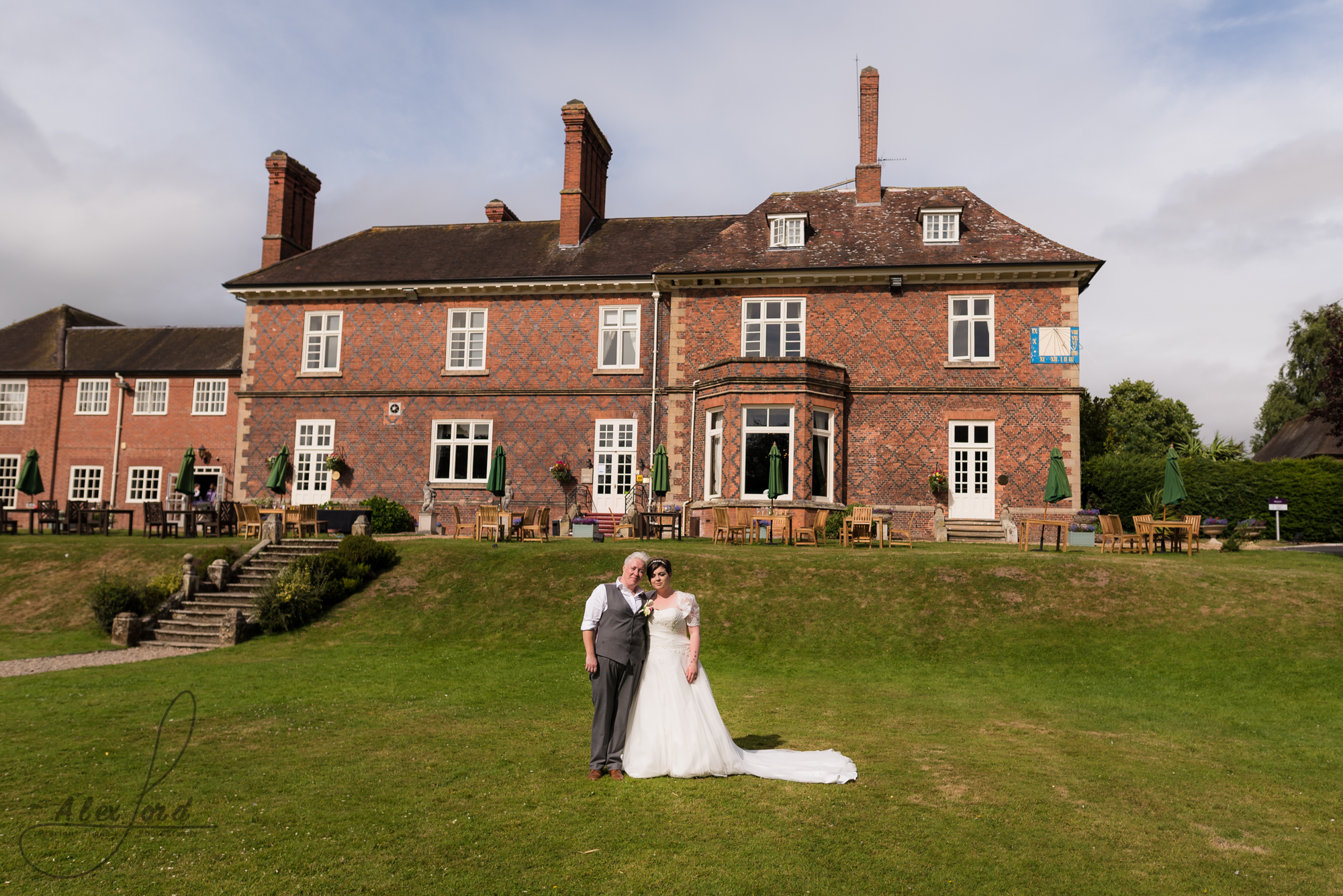 the bride and bride stand majestically in front of their wedding venue on a hot summers day