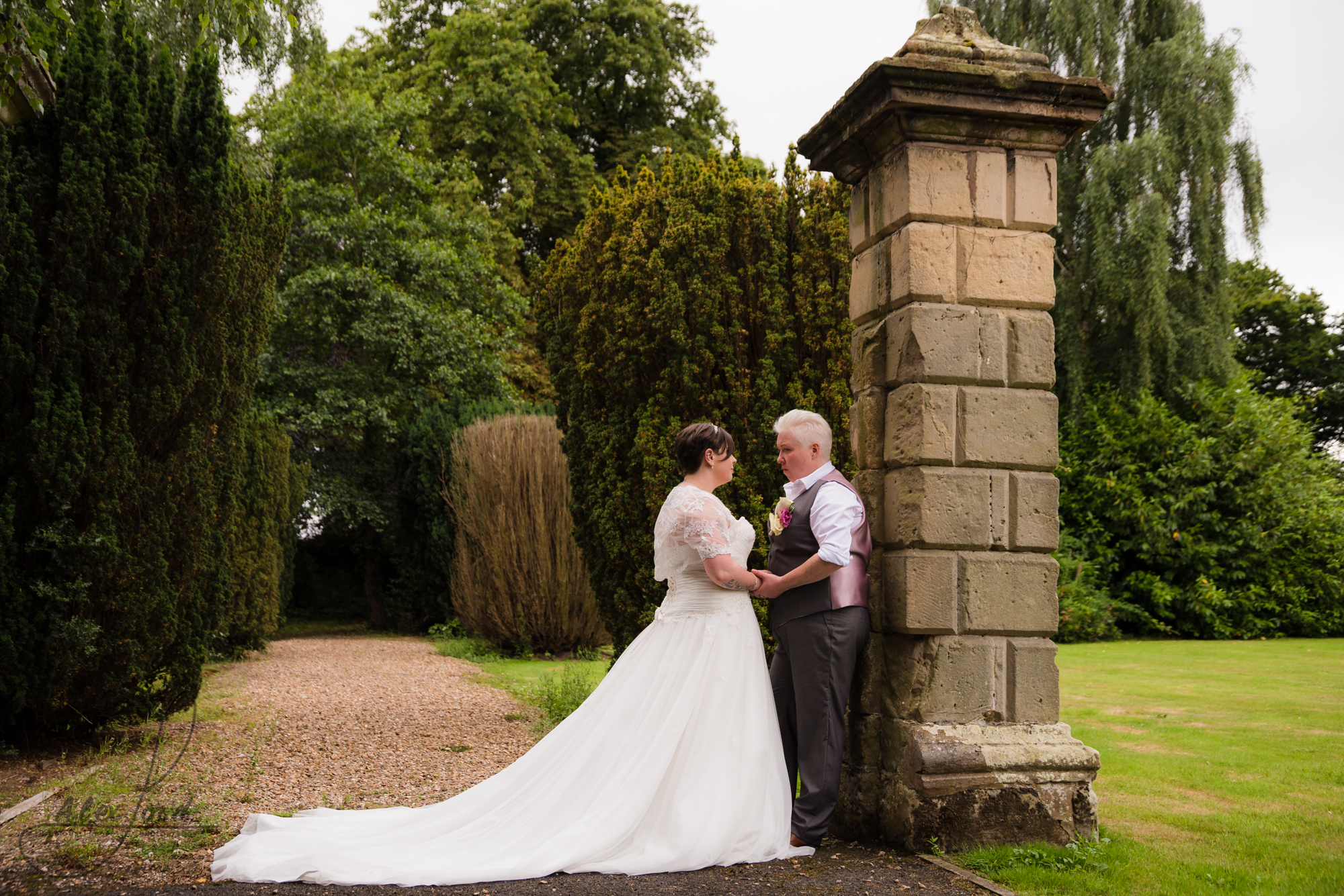 the bride and bride stand outside the gates of albrighton hall chatting together during their wedding photography