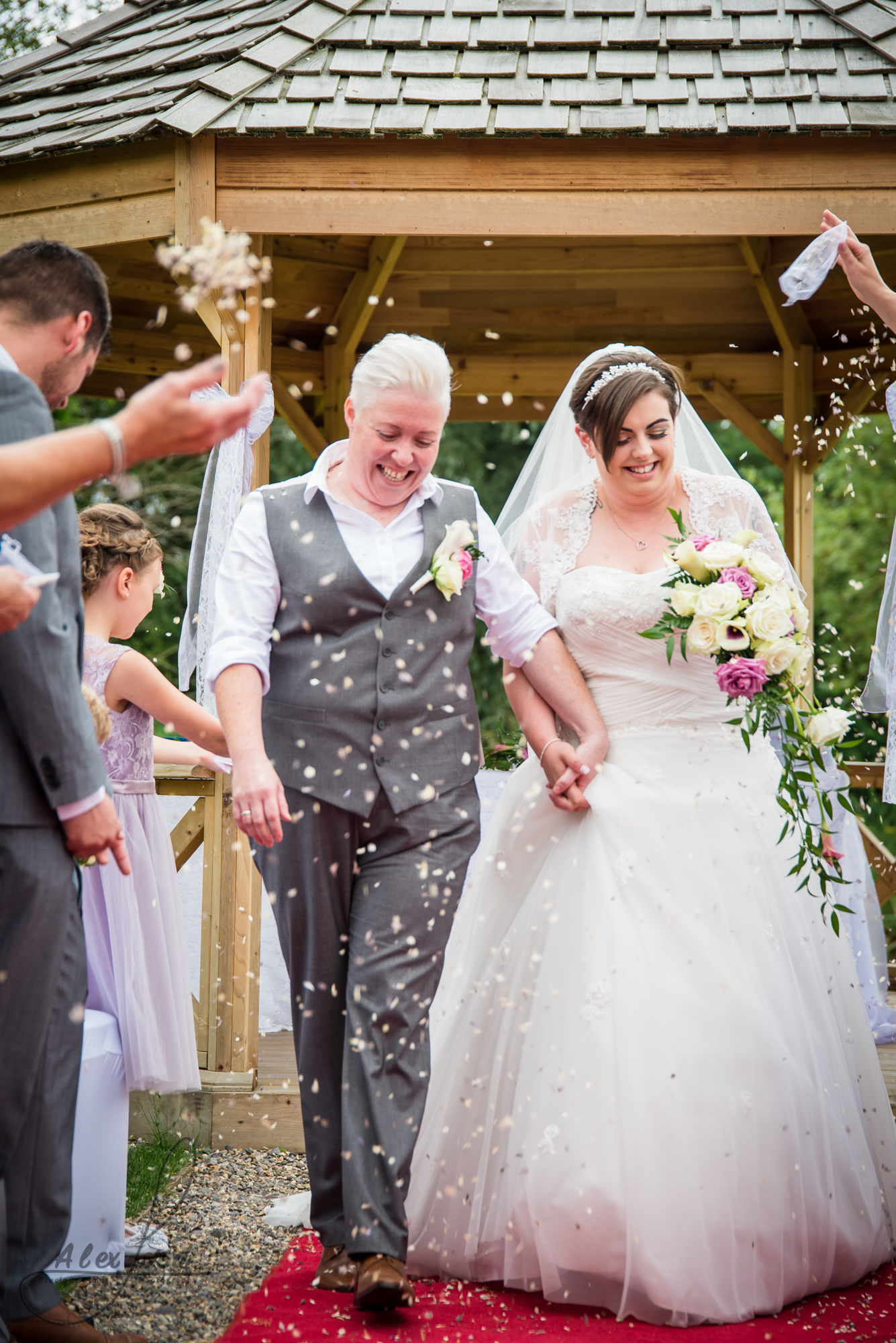 the bride and bride walk down the aisle together getting covered in confetti