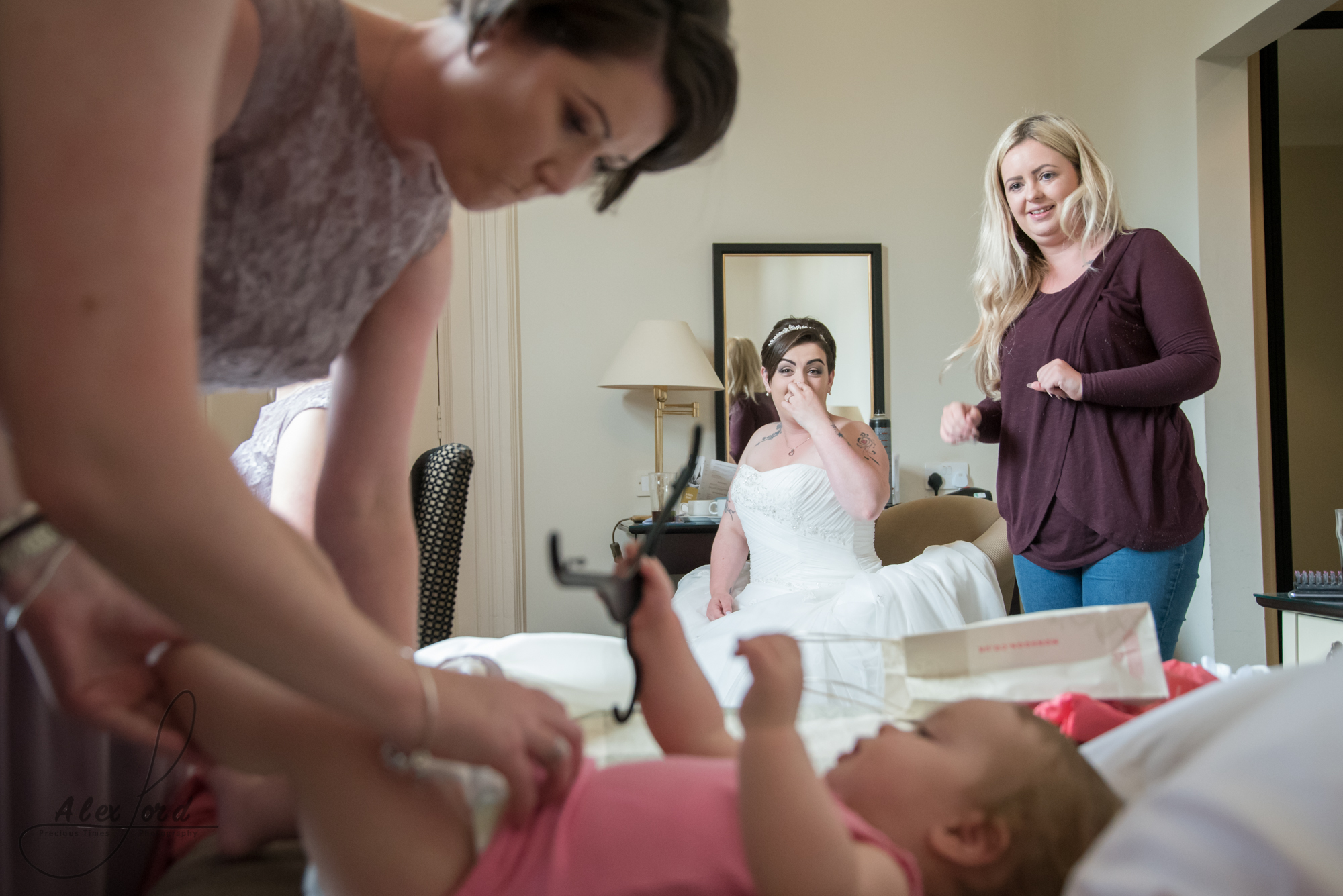 a bridesmaid changes the brides daughters nappy on the bed in the bridal suite