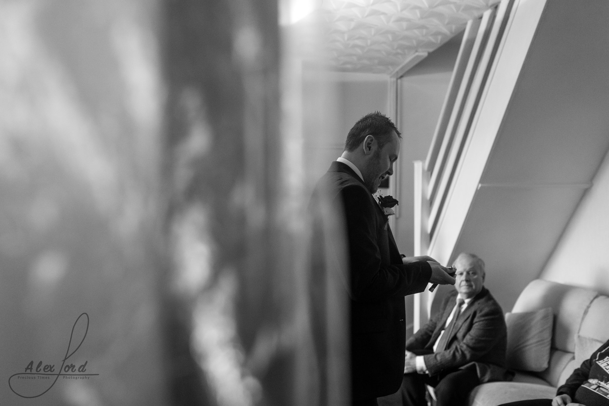 member of the groom party stands in the middle of the room, partly hidden by the door, while and elderly relative sits on the sofa