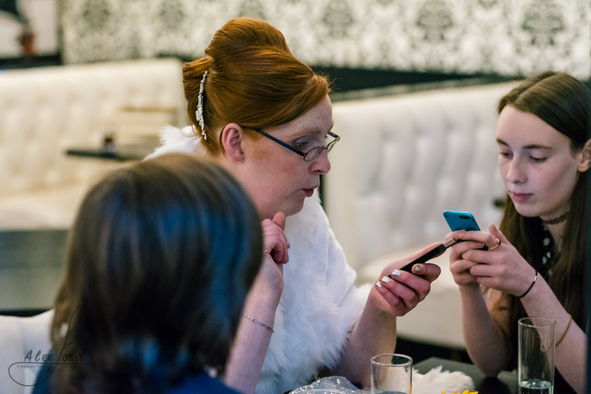 family members sit at a table during the reception and play on their phones